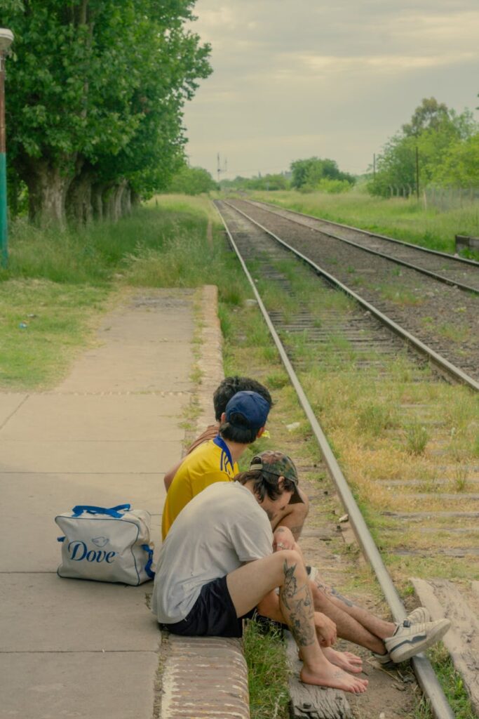 Three young adults sitting by rural train tracks in Argentina, embodying carefree summer vibes.